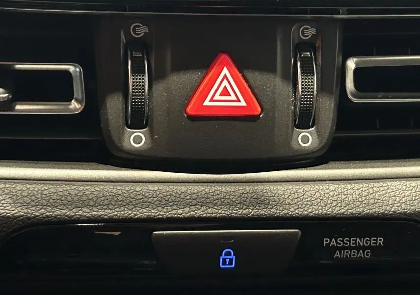 Gros plan sur la console centrale noire du Hyundai i30 SW 2022, mettant en valeur le bouton de warning rouge et les aérateurs.
