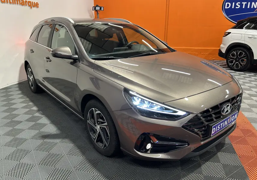 Hyundai i30 SW T-GDI 120CH Family en 3/4 avant gauche, couleur bronze métallique avec phares LED allumés.