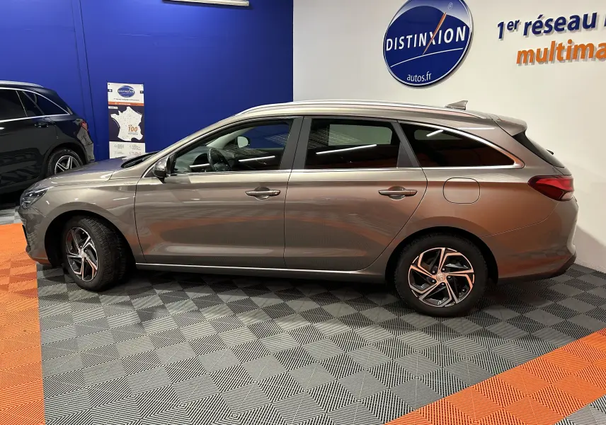Vue latérale droite d'une Hyundai i30 SW 2022 couleur bronze métallique, avec jantes alliage et vitres teintées, en intérieur showroom.