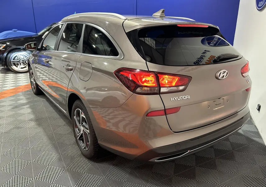 Vue 3/4 arrière droite d'une Hyundai i30 SW 2022 couleur bronze métallique avec feux arrière allumés en intérieur showroom.
