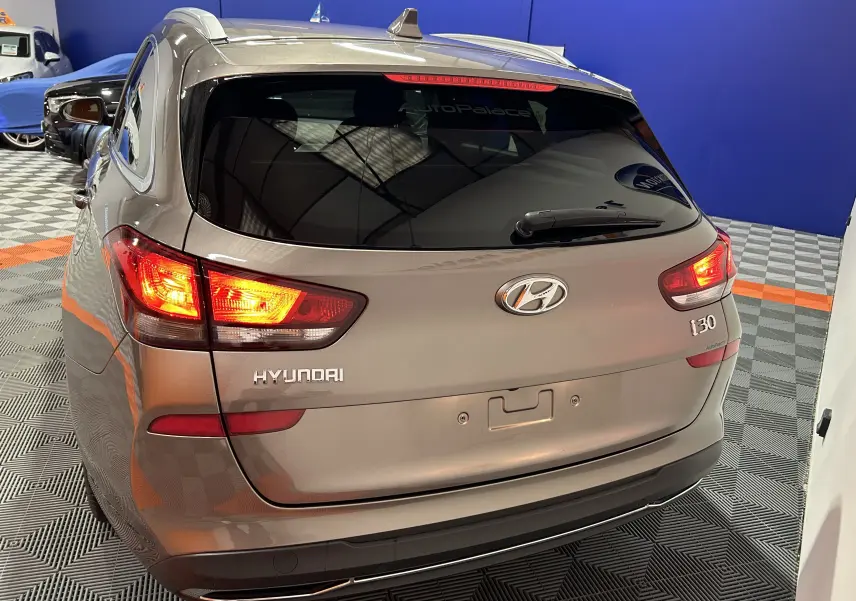 Vue 3/4 arrière gauche d'une Hyundai i30 SW 2022 couleur bronze métallique avec feux arrière allumés en intérieur showroom.