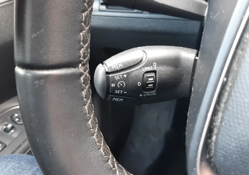 Gros plan sur la commande de régulateur de vitesse à gauche du volant en cuir noir du Peugeot 3008 gris Amazonite.