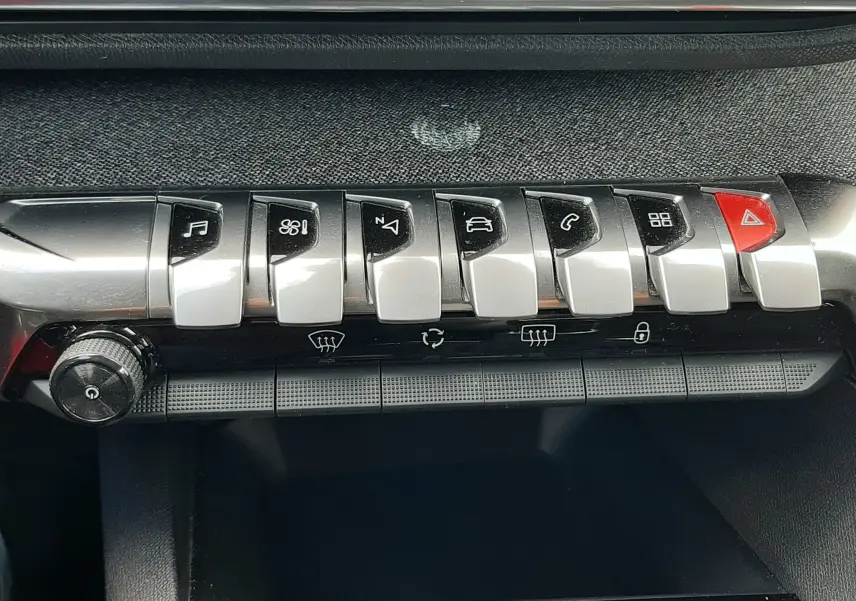 Gros plan sur la rangée de boutons chromés du tableau de bord du Peugeot 3008 gris Amazonite, avec bouton rouge d’alerte.