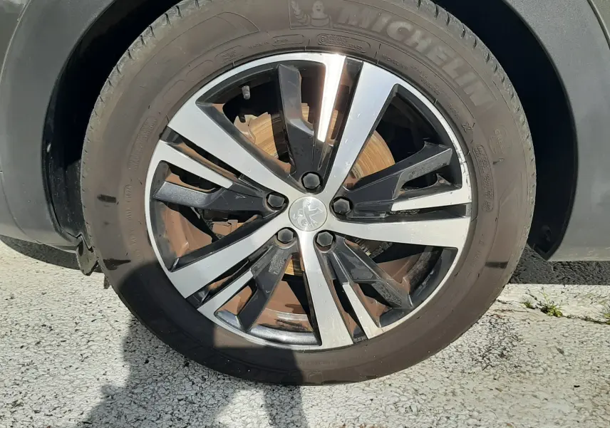 Gros plan sur la roue avant droite d’un Peugeot 3008 gris Amazonite avec jante alliage bicolore et pneu Michelin.