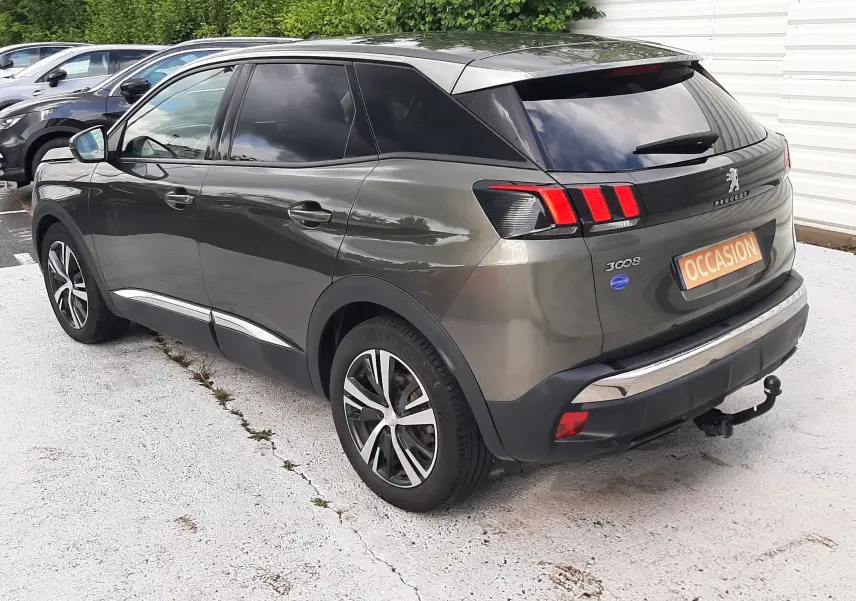 Peugeot 3008 gris amazonite vue 3/4 arrière droit, feux arrière à effet griffes et attelage visible.