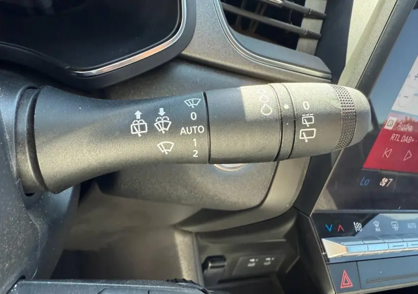 Gros plan sur la commande des essuie-glaces dans l’habitacle gris du Renault Captur 2025, écran tactile visible.