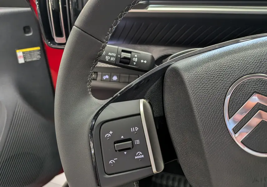 Gros plan sur le volant côté gauche du Citroën C3 Aircross rouge Elixir avec commandes intégrées et logo Citroën visible.
