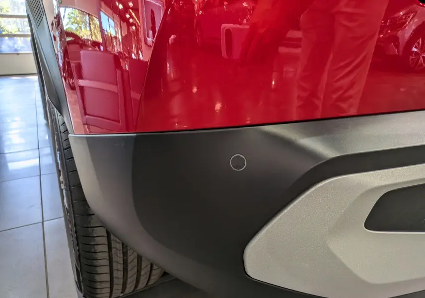 Détail du pare-chocs arrière gauche rouge Elixir du Citroën C3 Aircross hybride 2026 avec capteur de recul.