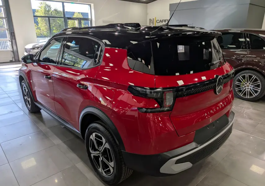 Vue 3/4 arrière droite du Citroën C3 Aircross hybride rouge Elixir avec toit noir et jantes bi-ton en showroom.