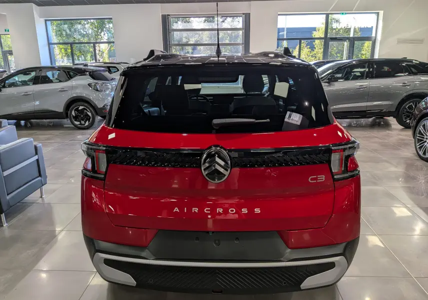 Vue arrière d'une Citroën C3 Aircross hybride rouge Elixir avec toit noir, en showroom lumineux.