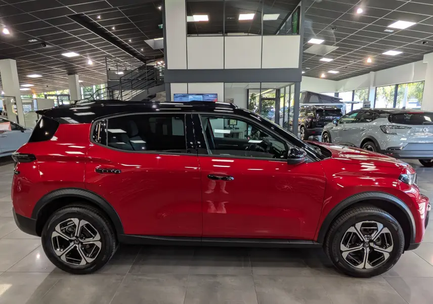Vue de profil côté gauche d'un Citroën C3 Aircross hybride rouge Elixir avec toit noir en showroom.