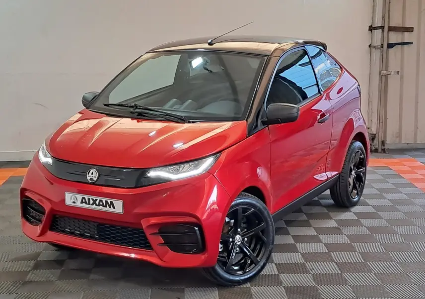Vue 3/4 avant d'une Aixam Ambition rouge 2025 avec toit noir et jantes noires brillantes dans un intérieur neutre.