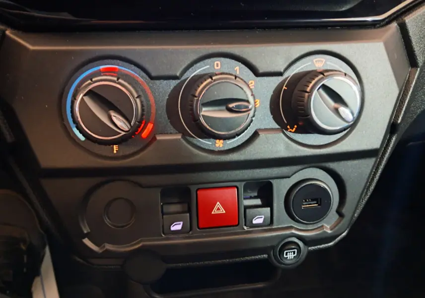 Tableau de bord de l'AIXAM AMBITION 2025 montrant les commandes de climatisation et les boutons de sécurité en gros plan.