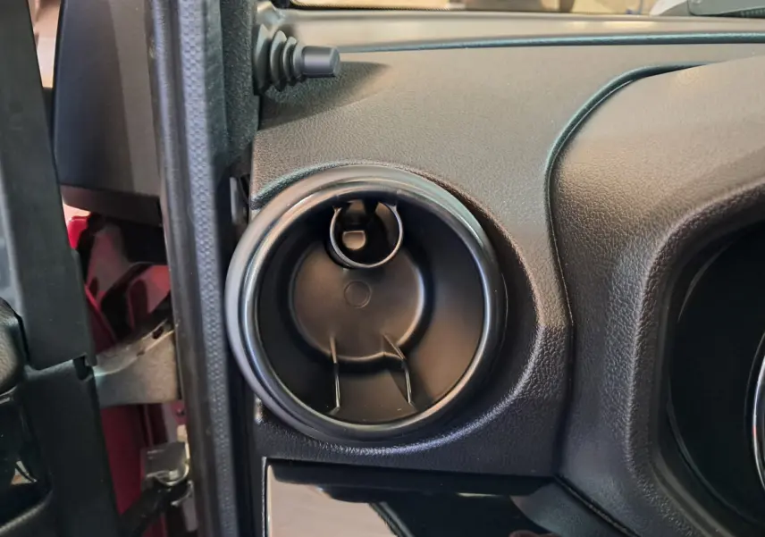 Gros plan sur la sortie d'aération ronde côté conducteur du tableau de bord noir d'une Aixam Ambition rouge.