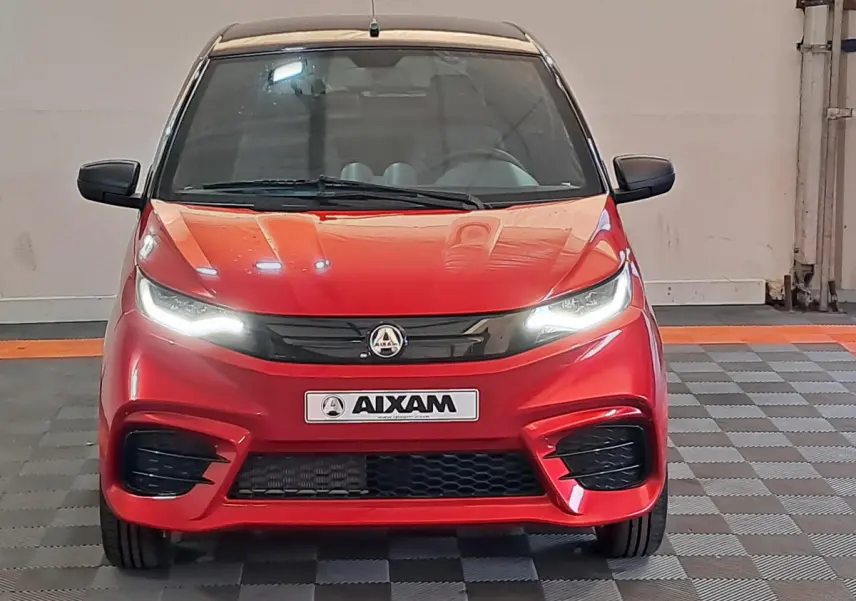Vue frontale d'une Aixam Ambition rouge 2025 avec phares allumés et calandre noire sportive.
