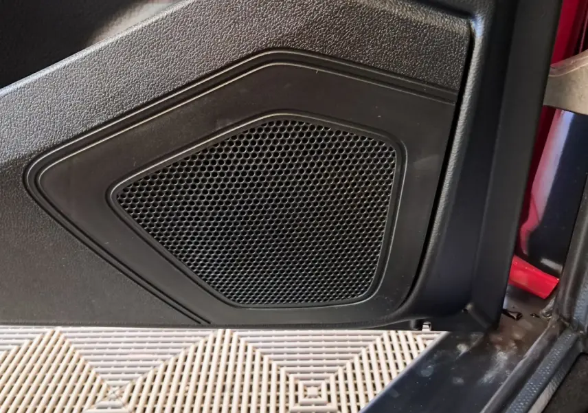 Gros plan sur le haut-parleur noir intégré à la porte côté conducteur d'une Aixam Ambition rouge 2025.
