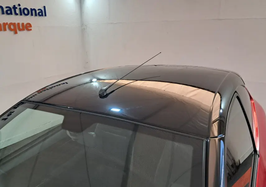 Toit noir brillant avec antenne vue en plongée sur une Aixam Ambition rouge, côté conducteur visible.