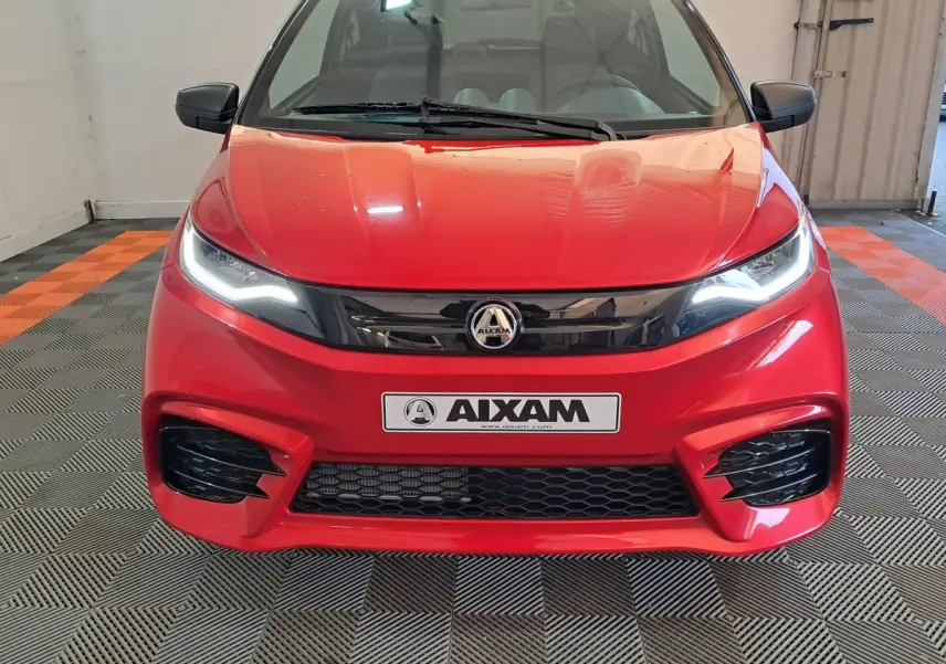 Vue frontale d'une Aixam Ambition rouge 2025 avec phares allumés et calandre noire brillante.