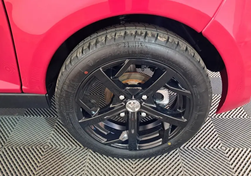 Gros plan sur la roue avant droite noire d'une Aixam Ambition rouge, mettant en valeur la jante sportive brillante.