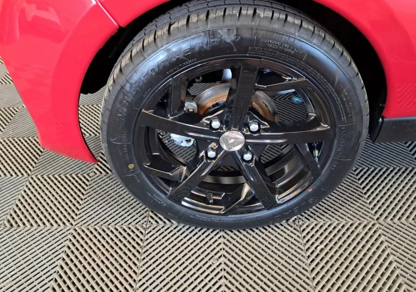 Gros plan sur la roue avant gauche noire brillante d'une Aixam Ambition rouge 2025 avec disque de frein visible.