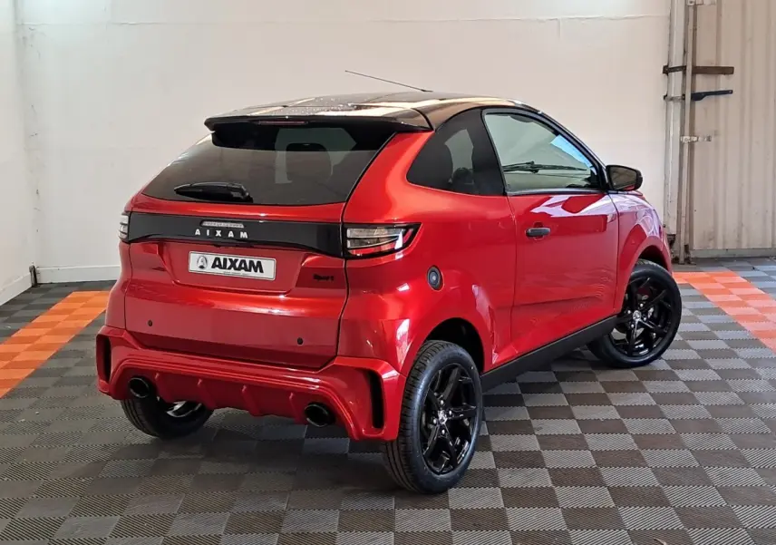 AIXAM AMBITION 2025 rouge vue 3/4 arrière droit avec jantes noires et toit noir brillant dans un garage.