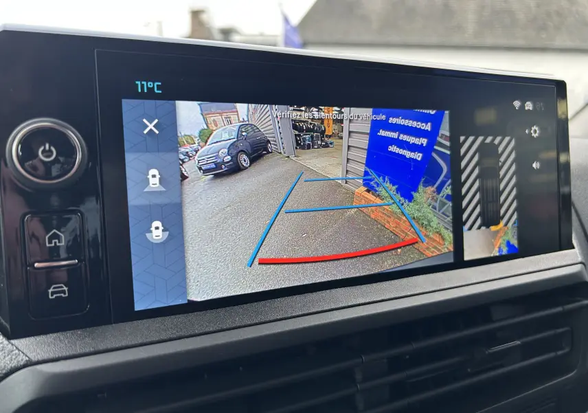 Écran tactile intérieur montrant la caméra de recul avec vue arrière sur une zone extérieure grise et un panneau bleu.