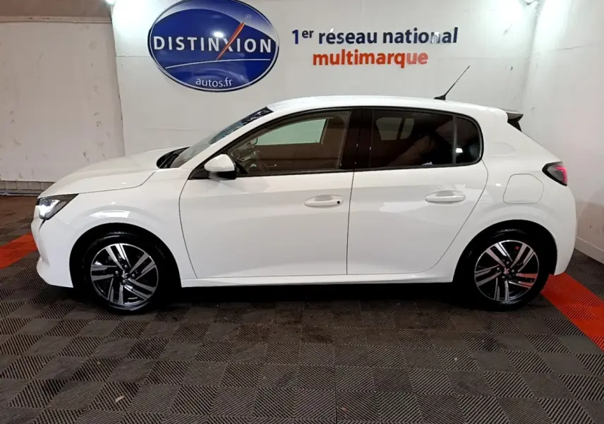 Profil côté gauche d'une Peugeot 208 blanche de 2021, avec jantes alliage et feux arrière LED visibles en intérieur showroom.