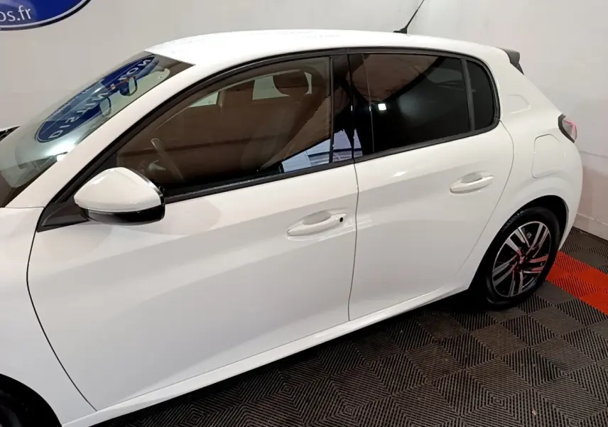 Vue de profil côté gauche d'une Peugeot 208 blanche, avec vitres teintées et jantes alliage distinctives.