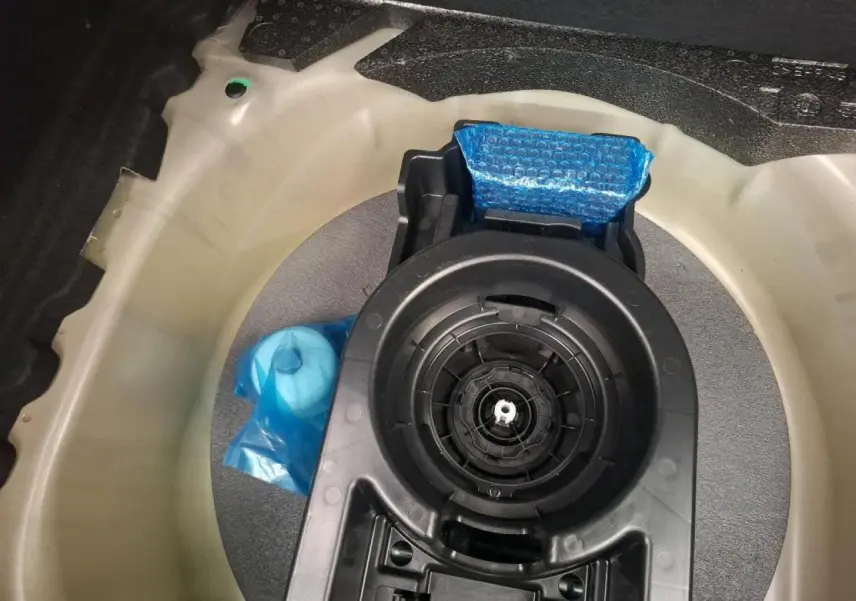 Vue plongeante sur le coffre d’un Peugeot 208 gris clair 2024, montrant le logement de la roue de secours et ses accessoires.