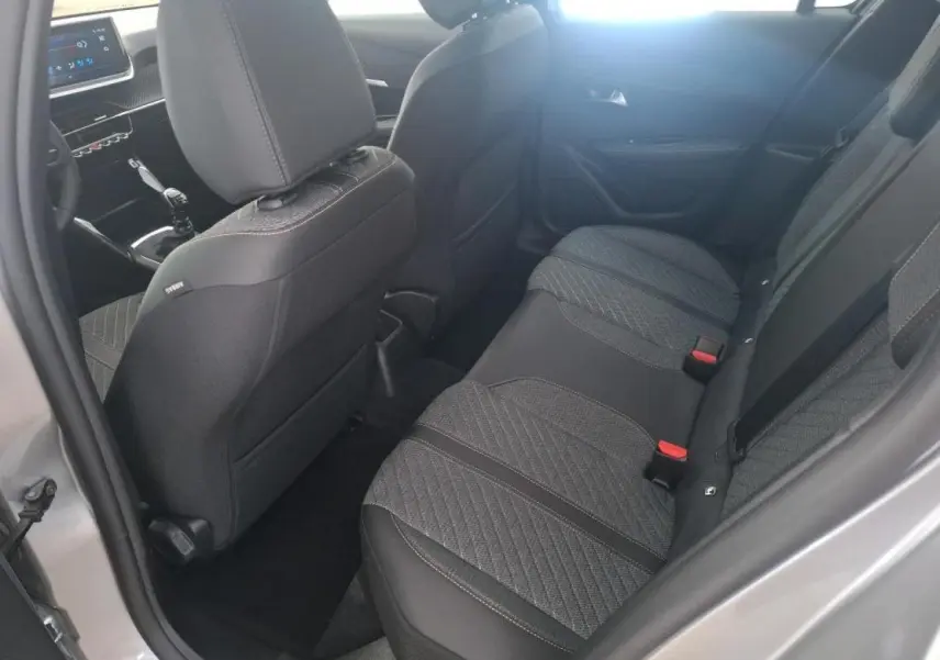 Vue intérieure arrière côté gauche de la Peugeot 208 2024 gris clair, montrant les sièges arrière et la console avant avec boîte manuelle.