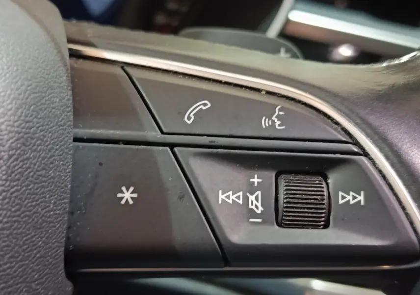 Gros plan sur les commandes vocales et volume au volant cuir noir de l'Audi Q3 Sportback gris foncé, version hybride rechargeable.