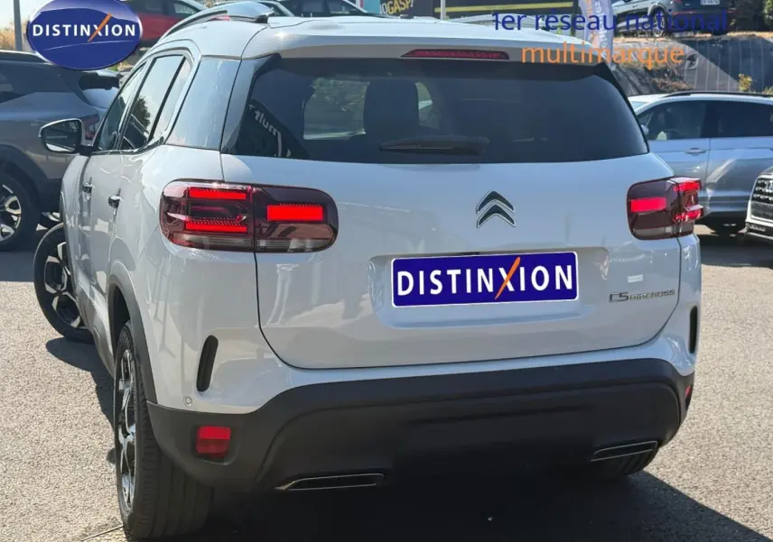 Vue 3/4 arrière du Citroën C5 Aircross blanc Okénite avec feux arrière LED et barres de toit visibles.