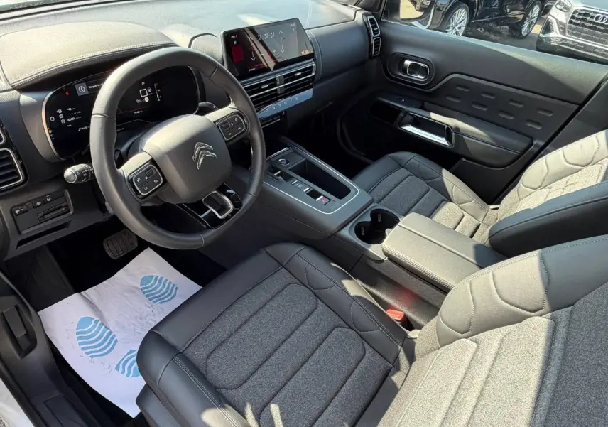 Vue intérieure côté conducteur du Citroën C5 Aircross 2025, avec sièges tissu noir et tableau de bord moderne.