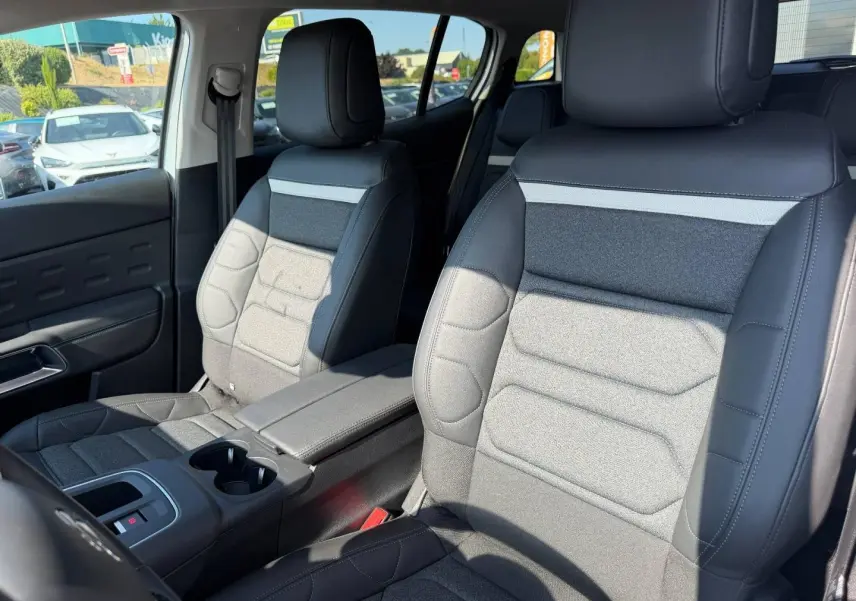 Vue rapprochée des sièges avant en tissu noir et gris du Citroën C5 Aircross 2025, avec accoudoir central et porte-gobelets.