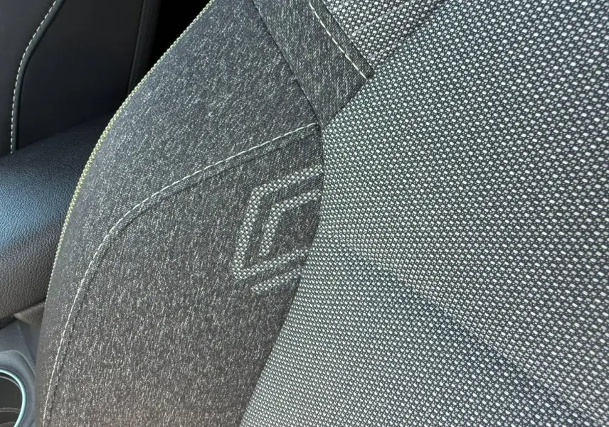 Gros plan sur le siège avant gris foncé du Renault Captur 1.6 E-Tech avec logo brodé et accoudoir en cuir noir.