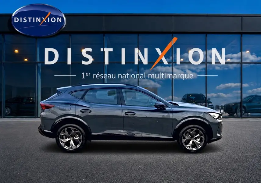 Vue latérale gauche du CUPRA Formentor 1.5 etsi hybrid 150 DSG7 en bleu fjord avec jantes 18 pouces devant un showroom Distinxion.