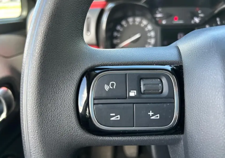 Gros plan sur les commandes audio au volant d'une Citroën C3 sable métal de 2021, intérieur noir.