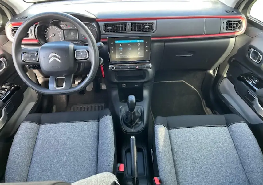 Vue intérieure avant de la Citroën C3 C-Series 2021, tableau de bord noir avec bande rouge et sièges gris bicolores.