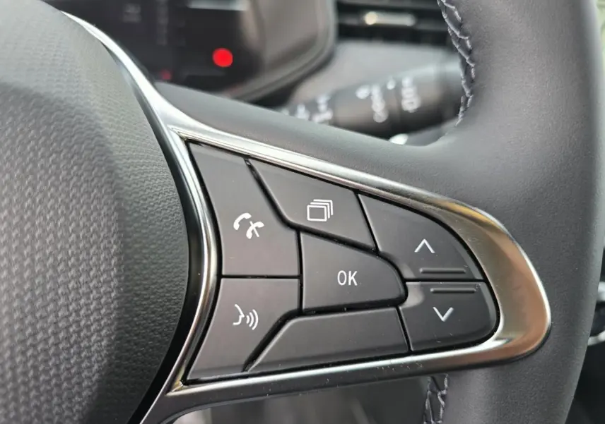 Gros plan sur les commandes multifonctions noires avec contour chromé du volant de la Renault Clio Gris Rafale Metal.