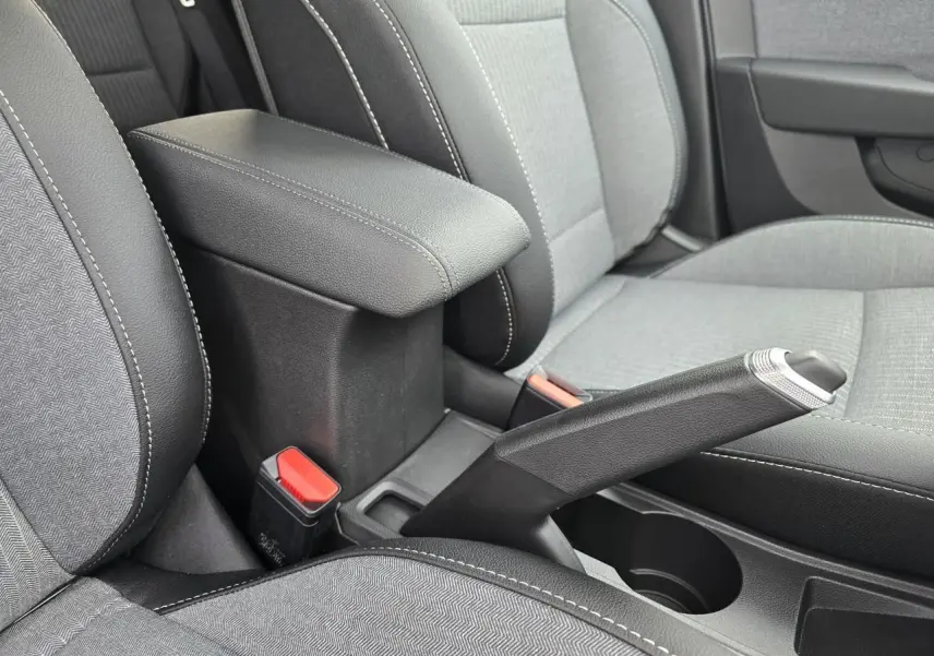 Vue rapprochée de l'accoudoir central coulissant et frein à main manuel entre les sièges gris clair et noir de la Renault Clio V.