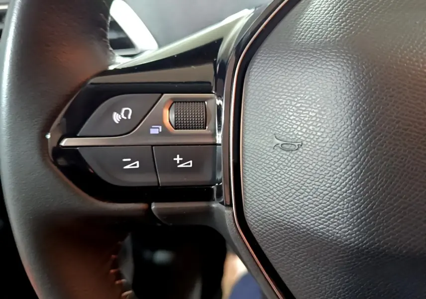 Gros plan sur le volant cuir noir du Peugeot 5008 2021, avec commandes multifonctions et bouton de volume.