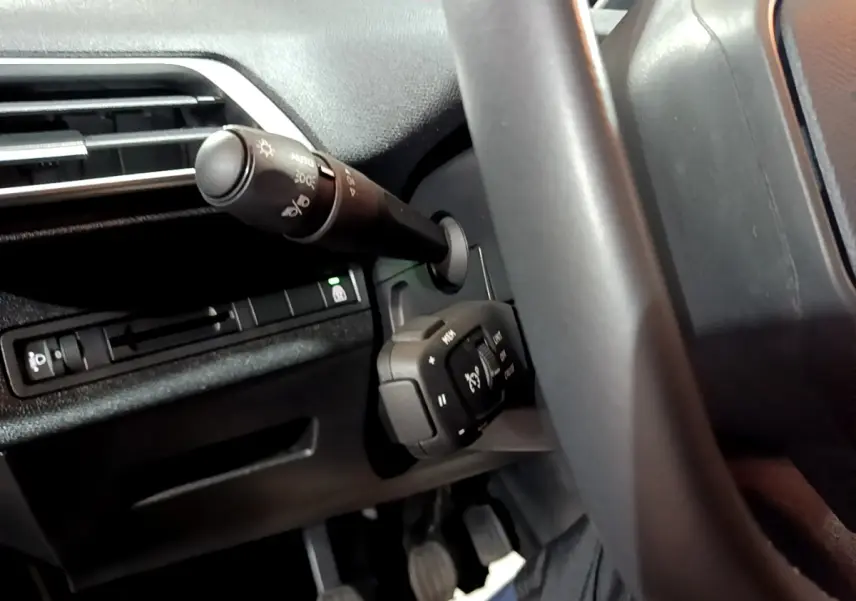 Gros plan sur la commande de régulateur de vitesse et les commandes d’éclairage du Peugeot 5008 noir, côté gauche du volant.