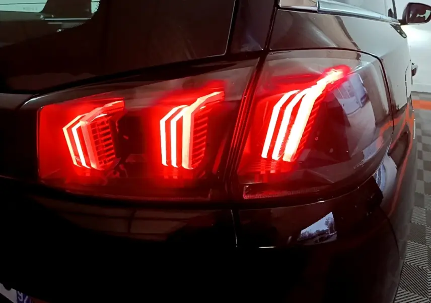 Gros plan sur le feu arrière droit rouge allumé d’un Peugeot 5008 noir, vue en légère plongée.