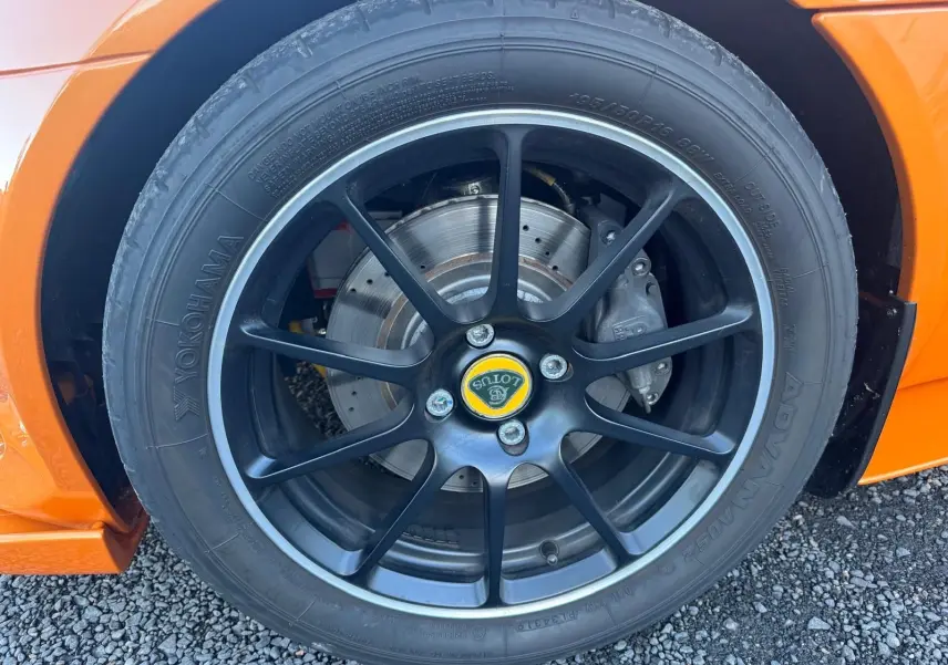 Gros plan sur la jante noire satinée forgée avec logo Lotus jaune, pneu Yokohama et partie orange de la carrosserie.