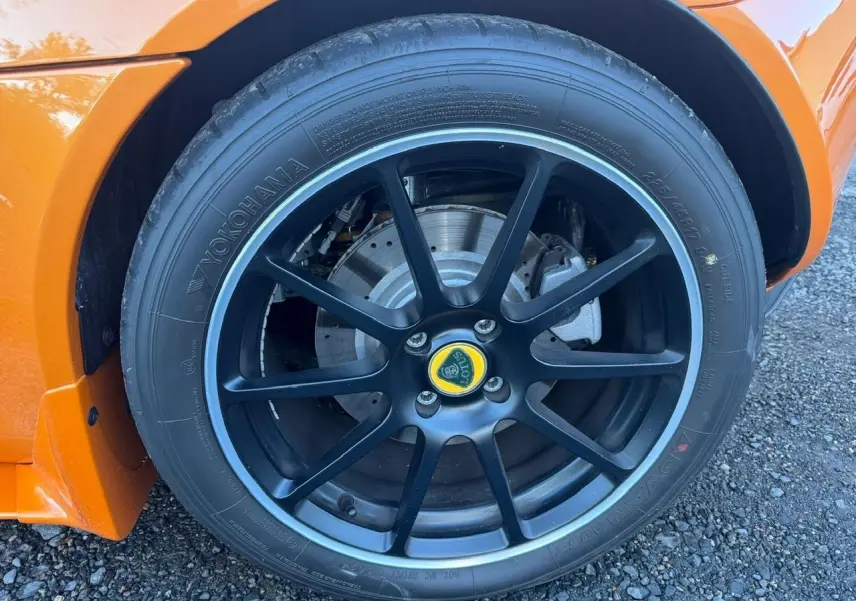 Gros plan sur la jante avant droite noire satinée de la Lotus Elise 3 Cup 250 orange, avec logo central jaune visible.