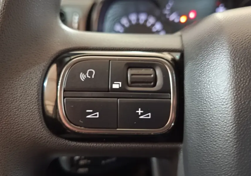 Gros plan sur les commandes noires du volant de la Citroën C3 blanche, avec boutons de volume et reconnaissance vocale.