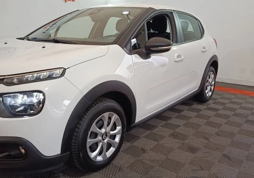 Vue 3/4 avant droit d'une Citroën C3 blanche avec phares distinctifs et jantes alliage en intérieur showroom.