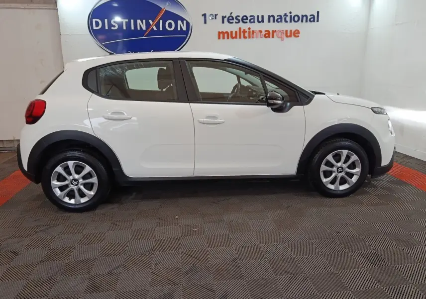 Vue latérale droite d'une Citroën C3 blanche de 2020, avec jantes alliage et logo Distinxion en arrière-plan.