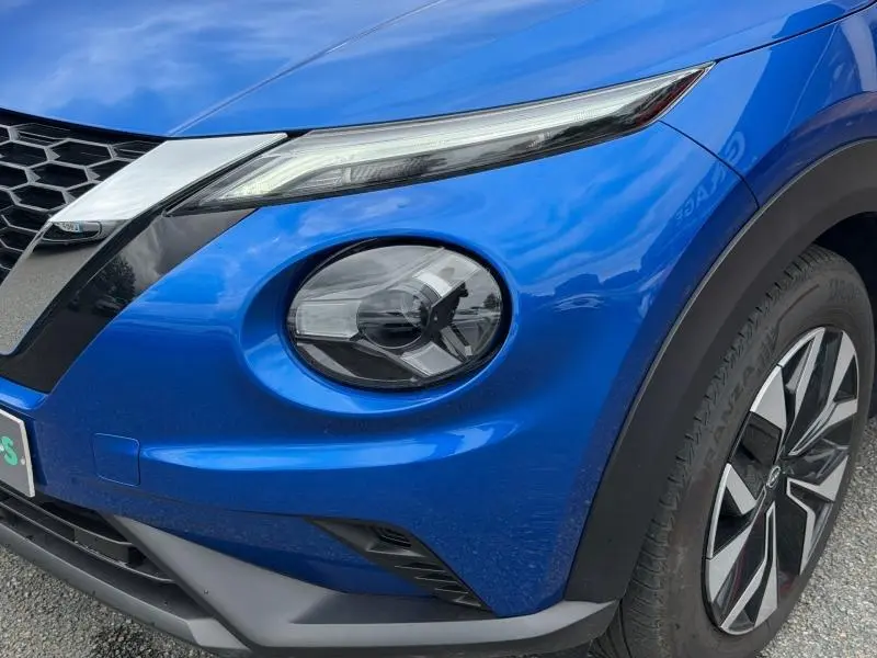 Gros plan sur l'avant droit bleu magnétique du Nissan Juke 2025, mettant en valeur le phare rond et la calandre noire.