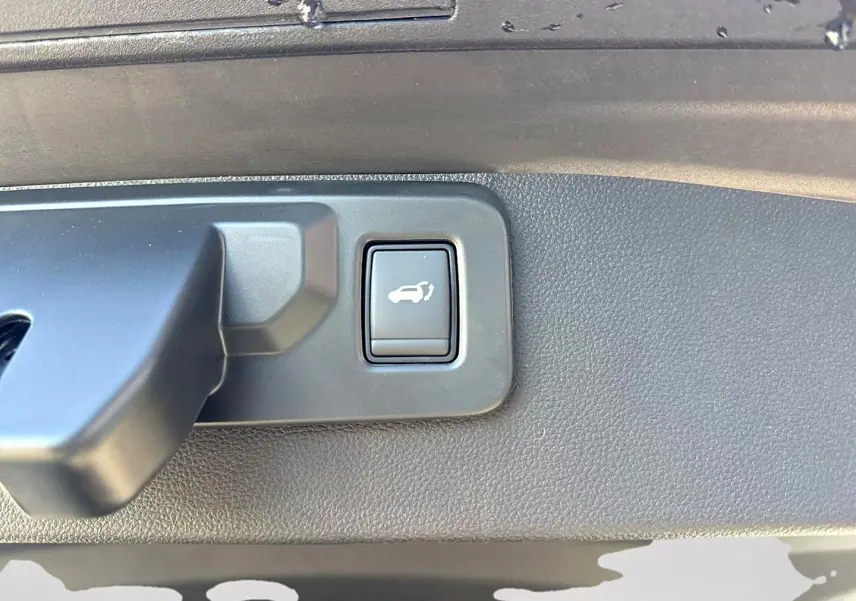 Gros plan sur le bouton d'ouverture électrique du coffre intérieur du Renault Symbioz gris rafale.
